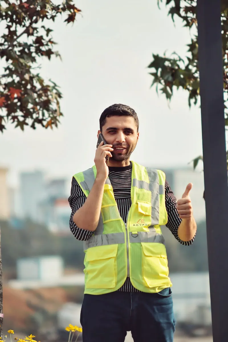 Contractor in a safety vest smiling while checking his phone on site